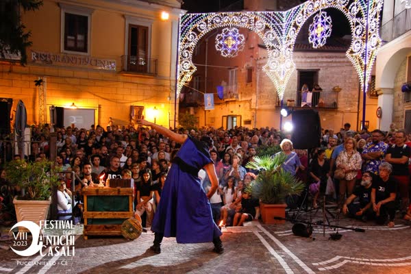 Alessandro con le bacchette da mangiafuoco e il braccio teso sotto le luminarie del borgo, Festival degli Antichi Casali 2023