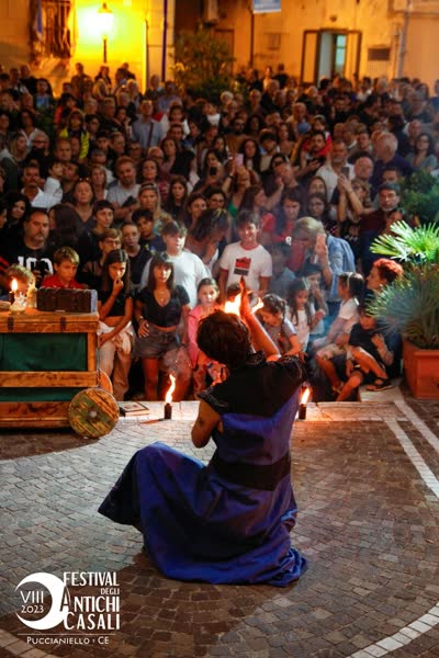 Alessandro in ginocchio davanti al carretto di scena di Athanor, con il pubblico intorno, Antichi Casali 2023